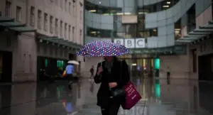 Una persona con ombrello davanti alla sede della BBC in una giornata piovosa