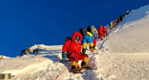 Alpinisti in tuta da alta quota affrontano una salita innevata sotto un cielo sereno