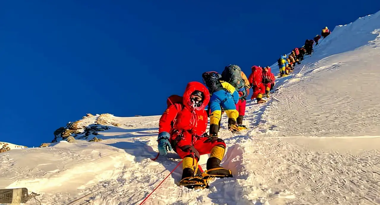 Alpinisti in tuta da alta quota affrontano una salita innevata sotto un cielo sereno