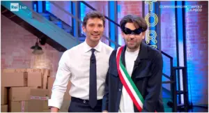 Due persone in uno studio televisivo, una indossa una fascia tricolore italiana