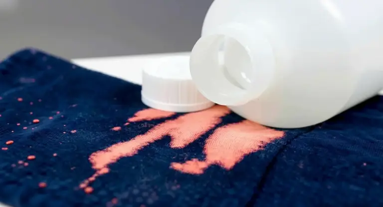 Macchie di candeggina su tessuto blu con flacone bianco rovesciato