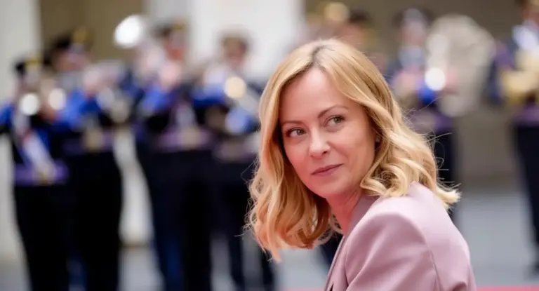 Una donna bionda in primo piano con un gruppo musicale sfocato sullo sfondo