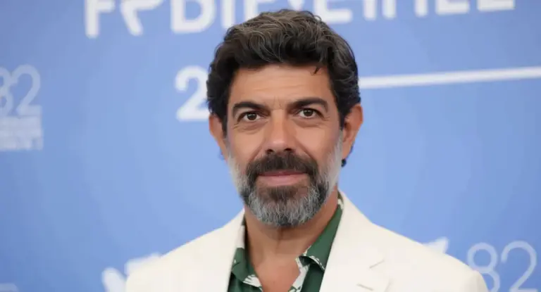 Un uomo con barba e capelli brizzolati su sfondo blu, in posa per una foto ufficiale