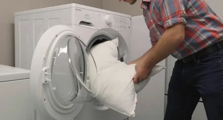 Persona inserisce un cuscino bianco in una lavatrice a carica frontale