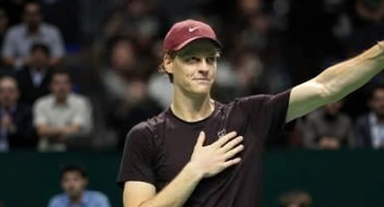 Un tennista saluta il pubblico con la mano sul petto durante un evento indoor.
